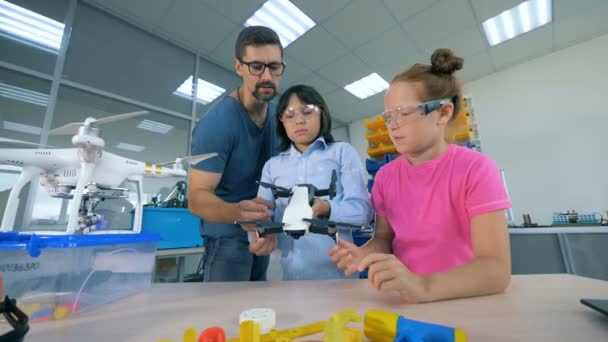One of two kids is holding a quadcopter and a specialist is instructing her about it — Stock Video