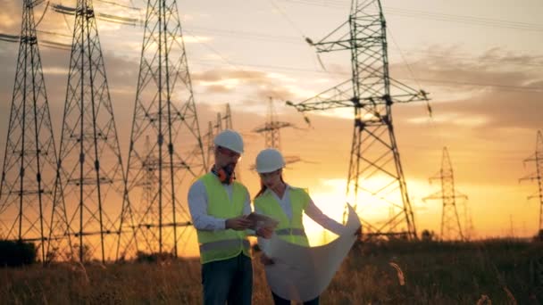 Deux ingénieurs en uniforme travaillent près des lignes électriques. Coucher de soleil fond . — Video