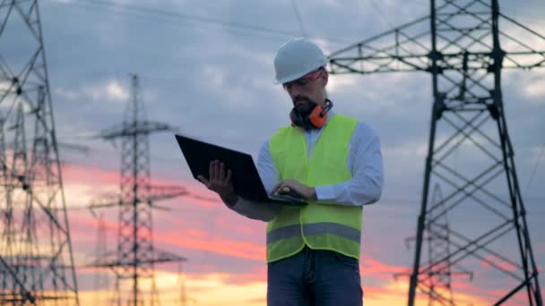 Profesionální elektrikář v jednotných typech v přenosném počítači při stání v blízkosti elektrického vedení. — Stock video