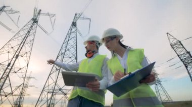 Mühendisleri bir tablet ile güç hatları üzerinde çalışır. Elektrik kabloları, güç trafo merkezi, elektrik alt istasyonlar, elektrik trafo merkezi kavramı.