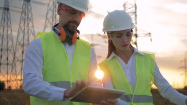 Elektrikçi işçiler inşaat plan günbatımı bir arka plan üzerinde tartışmak, yakın çekim.