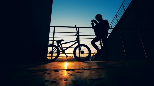Siluety mladého muže a jeho kolo v zapadajícím slunci — Stock video