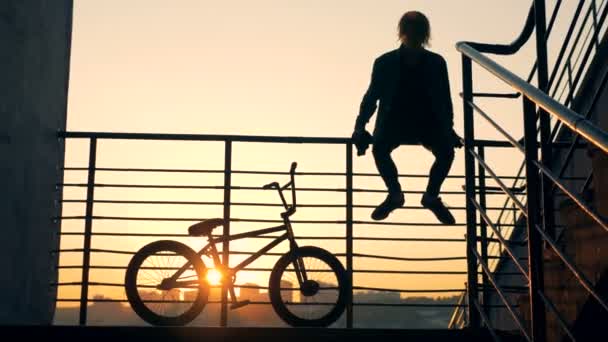 Fiatal férfi Ugrás a korlát, és elmegy a biciklijét során naplemente — Stock videók