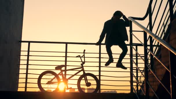 Trappa räcke med en manliga ungdomar som sitter på det och hans cykel bredvid honom — Stockvideo