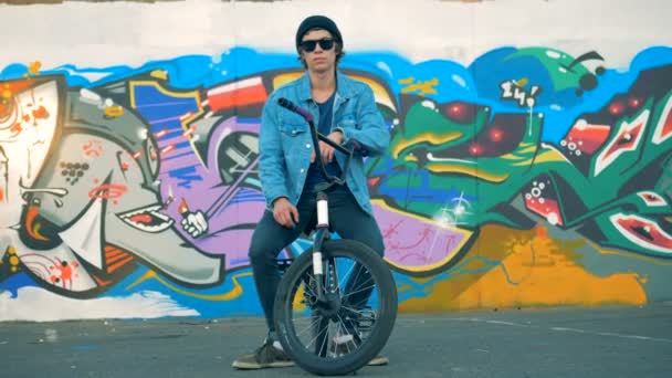 Mladý muž sedí na kole poblíž malované ulice zdi — Stock video