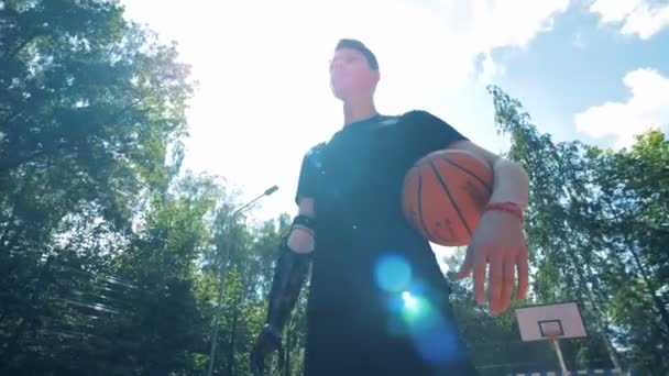 Wide angle view of a man with an artificial hand standing in a sports ground with a ball. — Stock Video