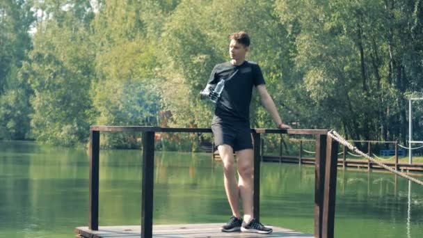 Flussbrücke mit einem jungen Mann, der darauf steht und mit seiner künstlichen Hand trinkt — Stockvideo