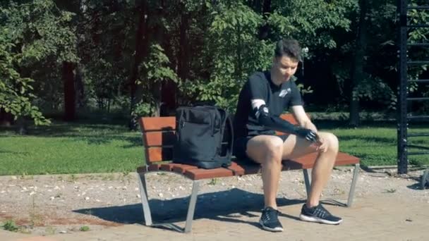 Adolescent avec une main bionique est assis sur un banc et commence à travailler sur un ordinateur portable. Concept futur . — Video