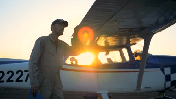 Um homem olhando para um biplano em um fundo por do sol, de perto . — Vídeo de Stock