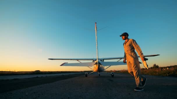 Piloto masculino va alrededor de un biplano, verificando su condición en una pista. 4K . — Vídeo de stock
