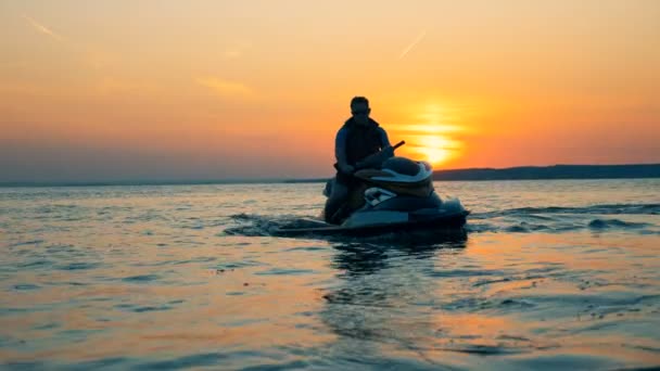 Cavaleiro senta-se em um jet ski em um fundo por do sol, close-up . — Vídeo de Stock