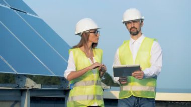 Yenilenebilir enerji kavramı. İki enerji çalışanı bir tablet ile bir güneş inşaat boyunca yürüyüş