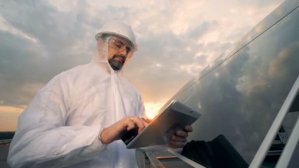 Мужчина в защитной одежде разговаривает на передатчике рядом с солнечной батареей — стоковое видео