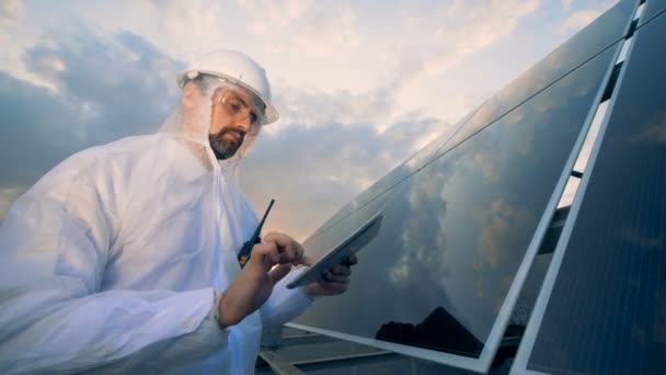 Trabajador energético está operando su tableta mientras está de pie junto a una instalación solar — Vídeos de Stock