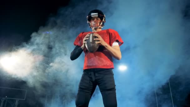 Американский футболист. Американский футболист стоит с мячом на темном облачном стадионе . — стоковое видео