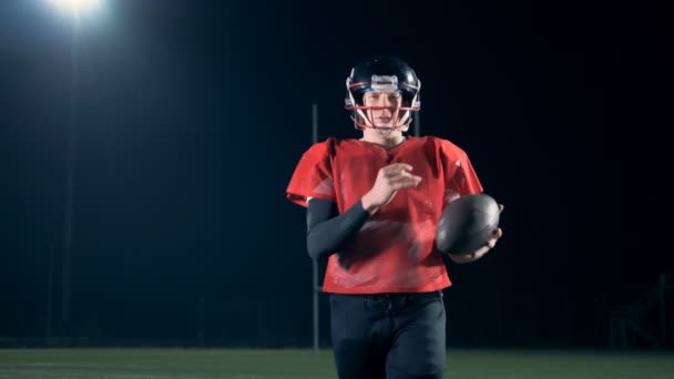 Il giocatore di football americano cammina su un campo da stadio con una palla in mano . — Video Stock