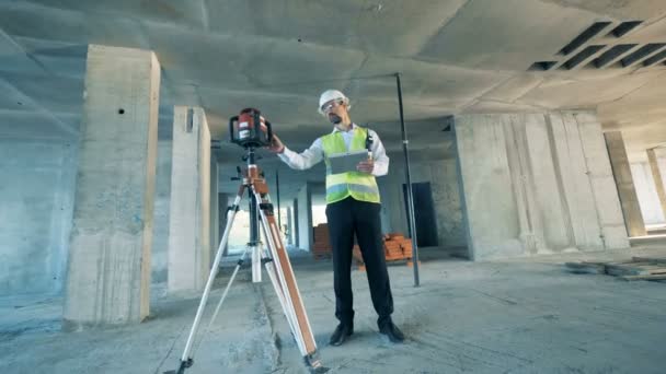 Construction worker is regulating land surveying equipment at a construction site — Stock Video