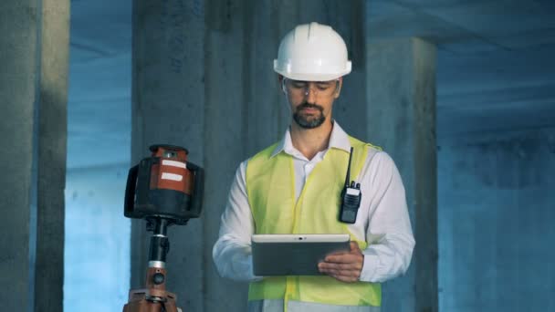 Arquitecto está sonriendo y mirando a la cámara mientras está de pie cerca de equipos de nivelación — Vídeo de stock