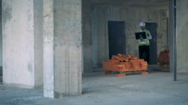 Erkek inşaat uzman elinde bir dizüstü bilgisayar ile inşaat alanı boyunca yürüyüş