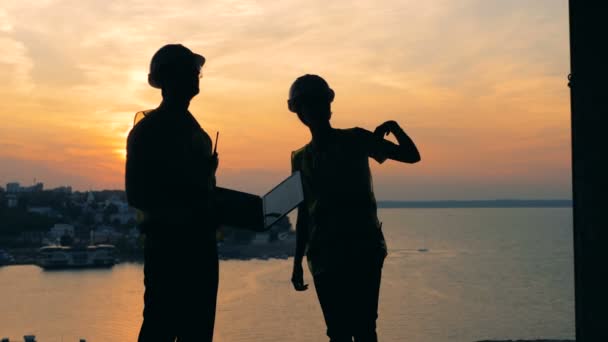 Un hombre y una mujer arquitectos, constructores, constructores están teniendo una conversación durante la puesta del sol — Vídeo de stock