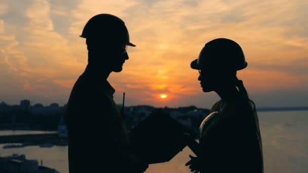 Nahaufnahme einer männlichen und einer weiblichen Arbeitersilhouette vor der Sonnenuntergangslandschaft — Stockvideo