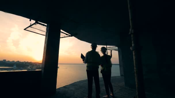 Dois especialistas em construção conversando em uma casa de construção no pôr do sol — Vídeo de Stock