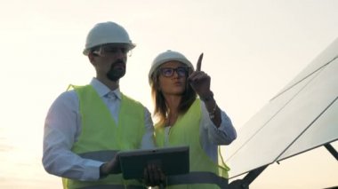 Mühendisler üniformalı bir tablet üzerinde birlikte, güneş panelleri duran yazın. Alternatif, yeşil enerji kavramı.