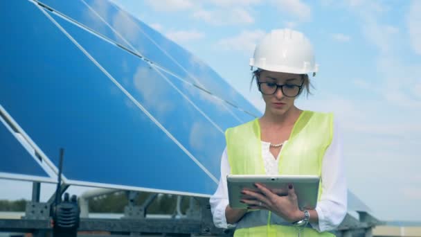 Ingeniera escribiendo en una tableta. Una mujer se para cerca de paneles solares, trabajando con una tableta . — Vídeos de Stock