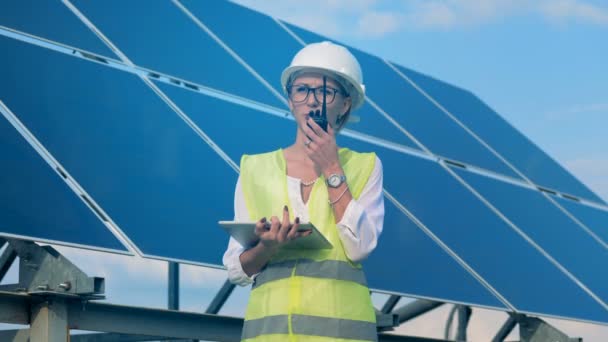Un ingeniero trabaja con dispositivos, de pie en un techo cerca de las baterías solares. Concepto alternativo de energía verde . — Vídeo de stock