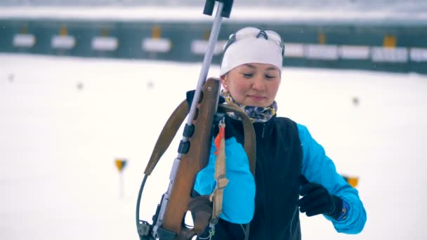 Een vrouw zet op een sport-pistool. Biatlon atleet neemt een pistool en zet het op een rug. — Stockvideo