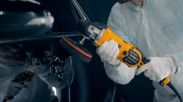 Een man een auto polijsten. Reparateur gebruikt polijsten apparatuur, werkt in een garage. — Stockvideo