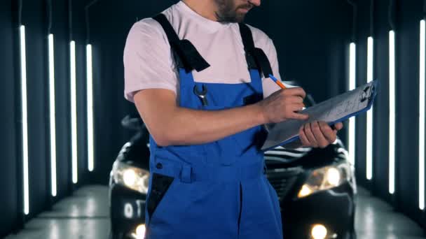 Механічний запис з ручкою на кишені. Чоловік стоїть в гаражі, пишучи на папері під час огляду . — стокове відео