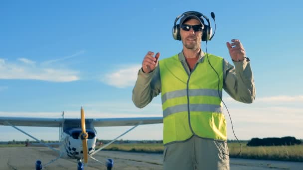 Ein Pilot steht auf einem Flugzeughintergrund. Mann mit Kopfhörer steht auf Startbahn. — Stockvideo