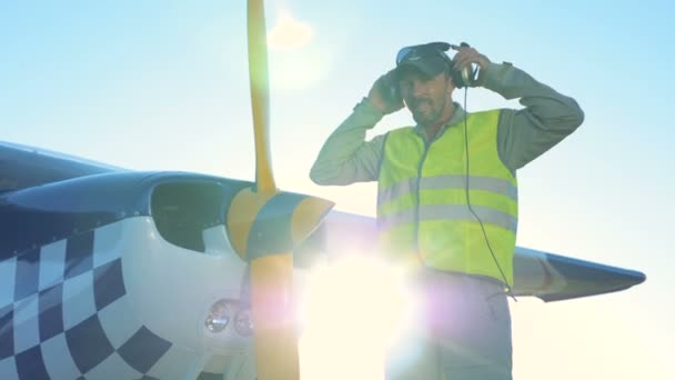 Mannelijke piloot staat in de buurt van een lichte privé vliegtuig. Een persoon staat in de buurt van een klein vliegtuig, op zoek en lachend op camera. — Stockvideo