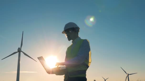 Ingenieur arbeitet an einem Sonnenuntergang Hintergrund. Windräder, grünes Energiekonzept. — Stockvideo