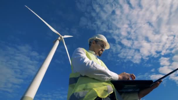 Ingenieur staat op de achtergrond van een wind turbine. Alternatieve energieconcept. — Stockvideo