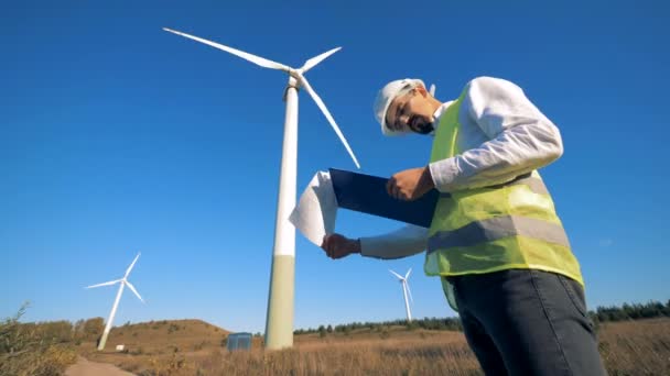 Bir kişi bir pano rüzgar türbinleri yürürken tutar. Yenilenebilir electririty, yeşil enerji kavramı. — Stok video