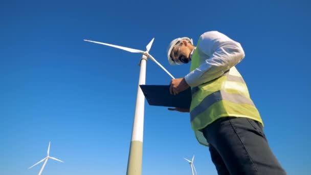 El trabajador está parado cerca de una turbina eólica, leyendo papel en un portapapeles. Electriridad renovable, concepto de energía verde . — Vídeo de stock