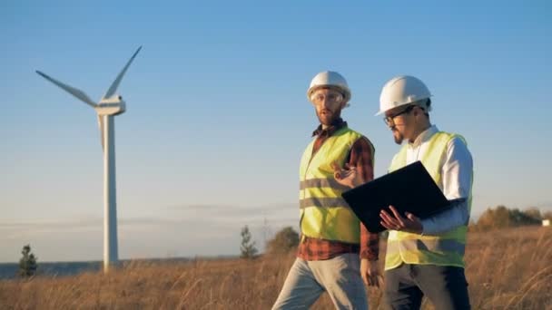 Los trabajadores revisan molinos de viento en un campo, caminando. Electriridad renovable, concepto de energía verde . — Vídeo de stock