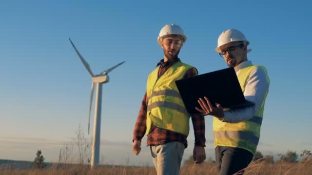 Männer diskutieren ein Projekt, während sie Windräder auf dem Feld überprüfen. Umweltenergiekonzept. — Stockvideo