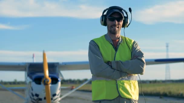 Un piloto sonriente está de pie cerca de un biplano en el campo — Vídeo de stock