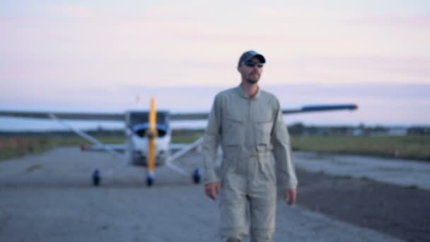 Male aviator is walking away from a biplane and stops with a smile — Stock Video