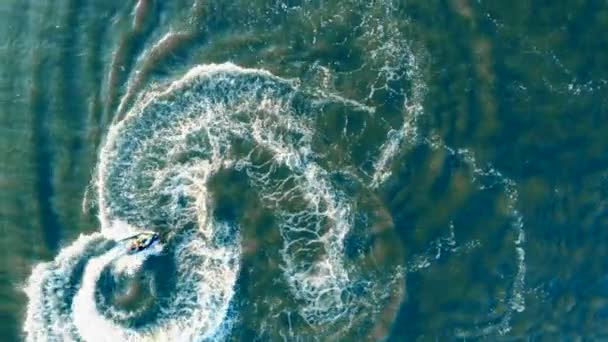 Percikan dan gelombang terbentuk setelah sebuah skuter air berlayar melintasi laut dalam pandangan dari atas — Stok Video
