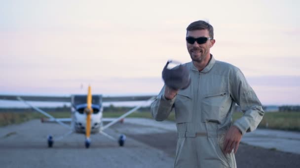 Cheerful pilot is putting on a cap while standing beside an aircraft — Stock Video