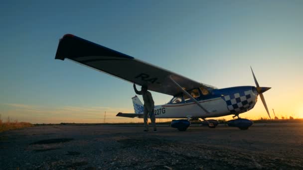 Крыло самолета осматривает мужчина-летчик на фоне заката — стоковое видео