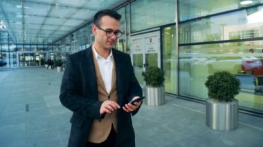 Erkek Müdürü bina boyunca yürüyüş ve bir gülümseme ile bir akıllı telefon işletim. 4k