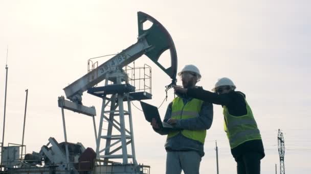 Ingenieurs werken aan een veld, staande in de buurt van een olie-toren. Olie productie industrie concept. — Stockvideo