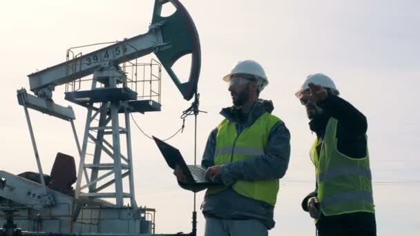 Ingénieurs parlant sur un champ avec des tours pétrolières. Concept d'industrie d'extraction pétrolière . — Video