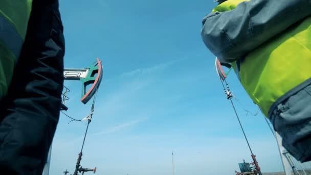 Trabajadores masculinos discutiendo un proyecto cerca de plataformas petrolíferas, de cerca . — Vídeo de stock