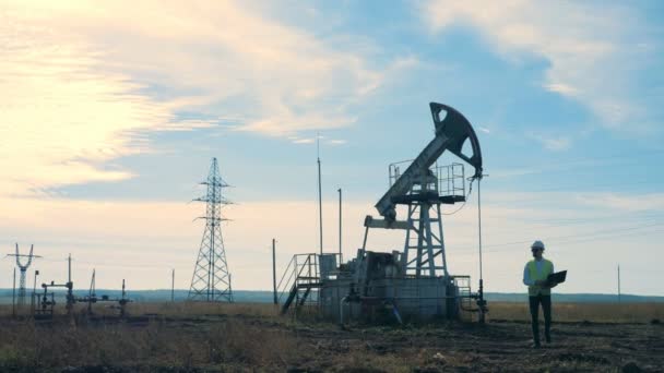 Un homme marche sur un champ avec des derricks de pétrole. Concept d'industrie d'extraction pétrolière . — Video